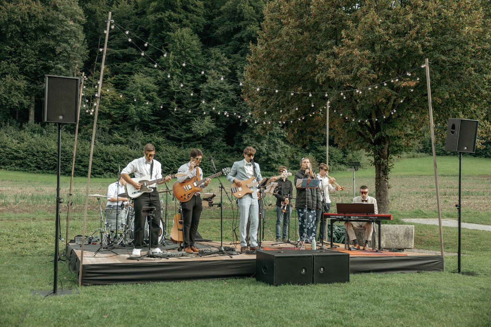 Liveband auf einer Bühne im Freien mit Lautsprechern, Subwoofern und Lichterketten an einer Hochzeit